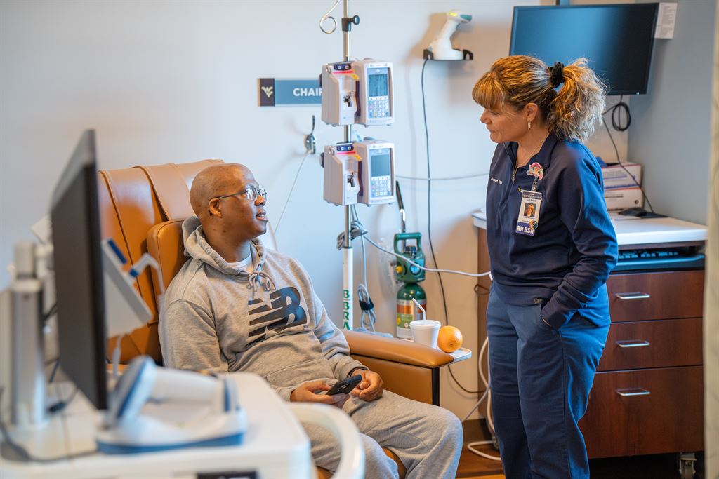 A man, Charles Walker, sits in a chair at the WVU Cancer Institute at Berkeley Medical Center, speaking to a care provider.