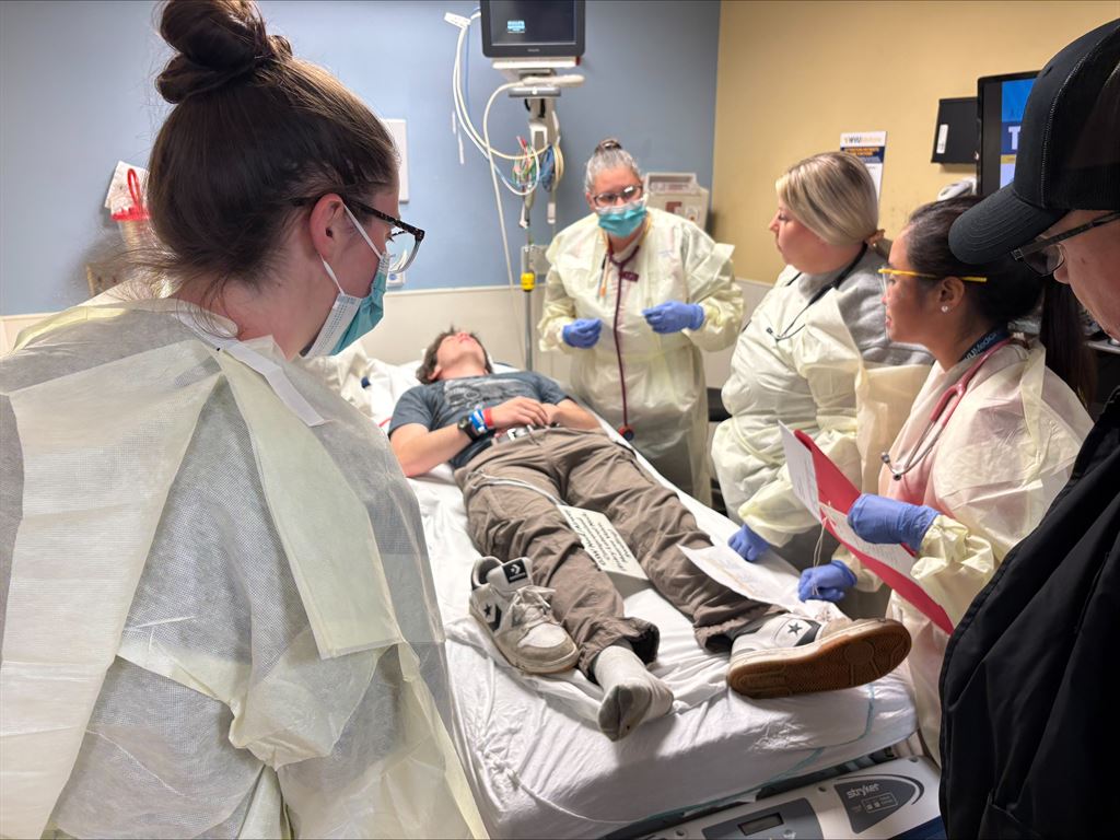 Providers gather over a bed with a drill participant portraying an emergency victim.