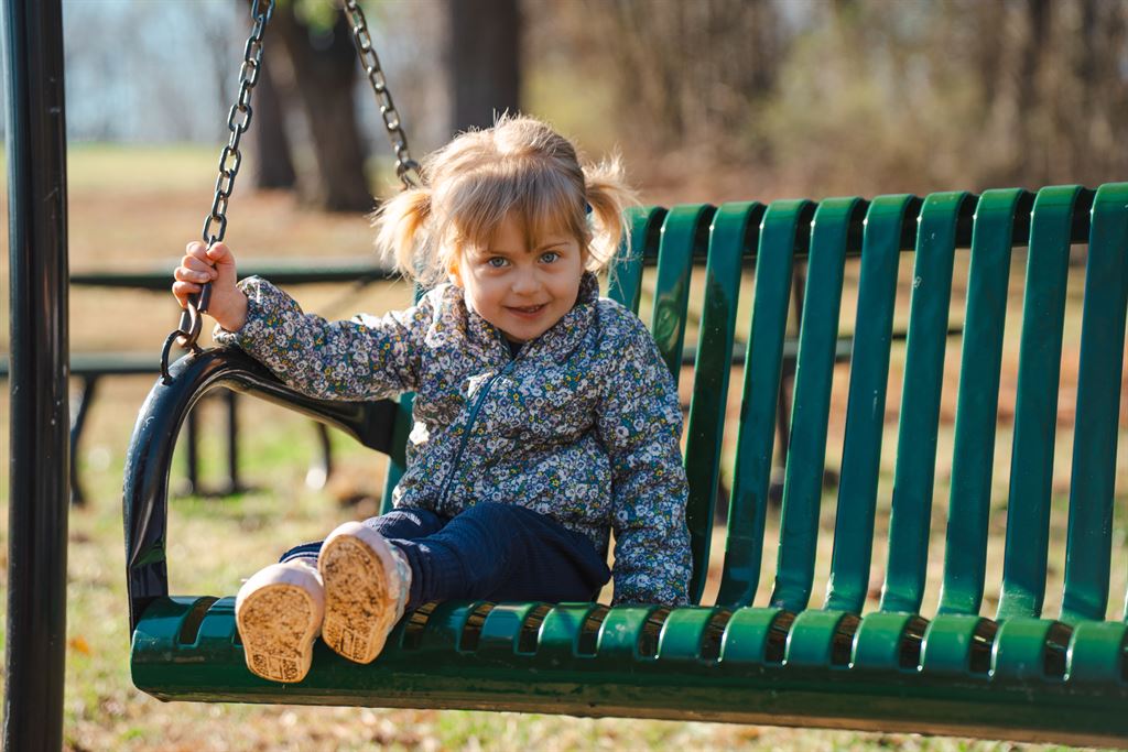 A toddler who received care from WVU Medicine Golisano Children's sits on a swing at a playground.